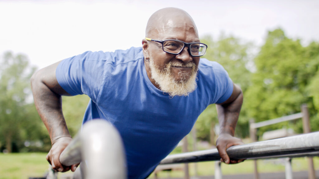 Healthy senior black male doing push ups on bars outdoors